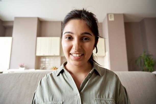 istockphoto-1262283010-612×612 Smiling indian woman online teacher, sales agent, remote tutor or call center operator wearing headset look at webcam app conference video call at home office. Headshot portrait. Webcamera view.